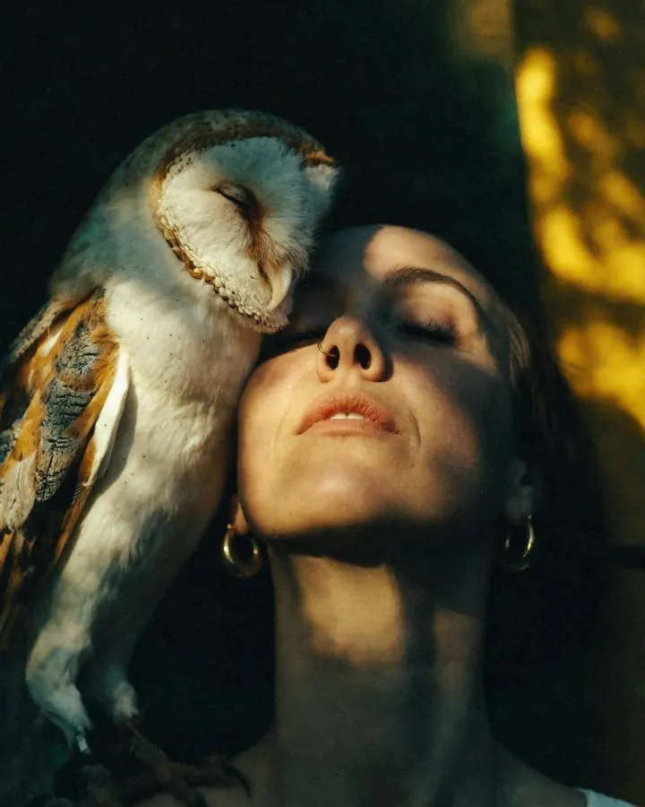Emma with her eyes closed and a barn owl resting against her cheek