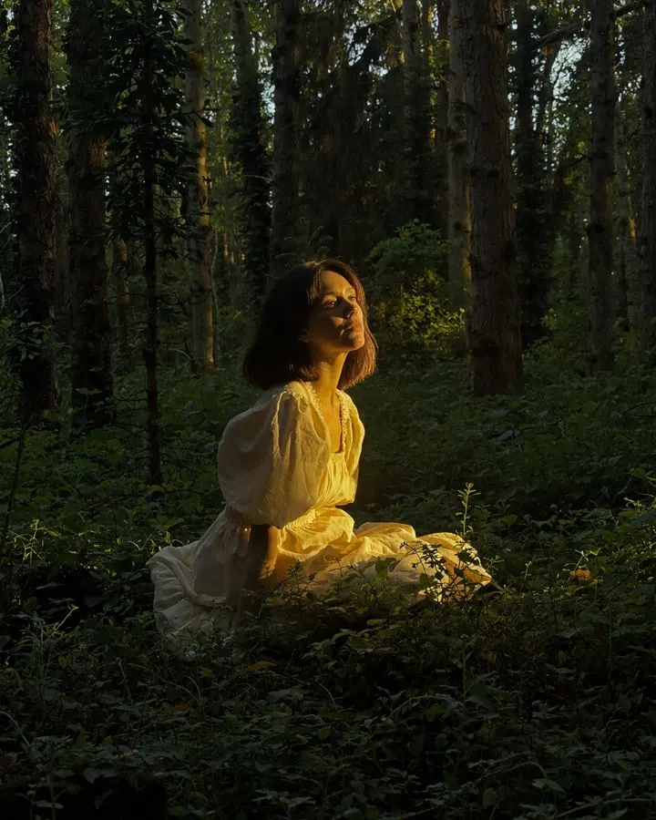 Emma sitting in a dark forest, lit by a shaft of warm light