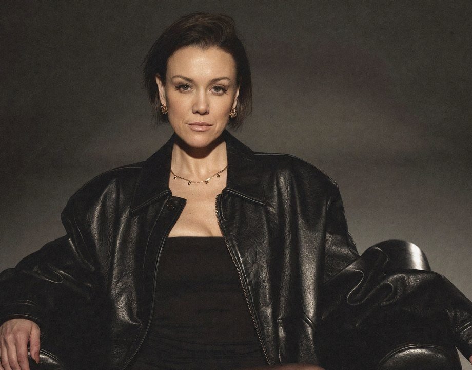Emma Armstrong in an oversized black leather jacket, sitting in a leather armchair, looking straight at the camera